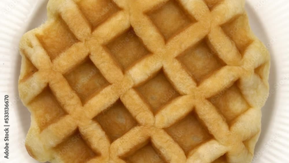 Top view rotation of delicious homemade fresh baked single round waffle in white ceramic dish. Top view rotation of delicious homemade fresh baked single round waffle in white ceramic dish.