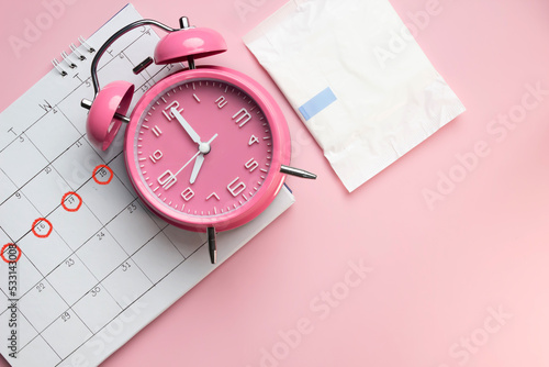 Women's menstruation Calendar, sanitary napkin in a package with pink alarm clock on a pink background. The concept of critical days time. photo