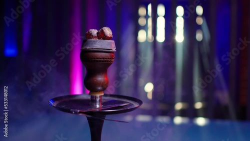 a close-up hookah bowl with coals, a beautiful hookah that smokes stands in a hookah room in a muted blue light.