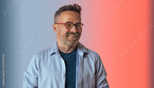 Portait of handsome European elderly man smiles positively enjoys life in blue shirt and spectacles has perfect white teeth isolated over blue pink studio wall. Cheerful mature attractive male indoor