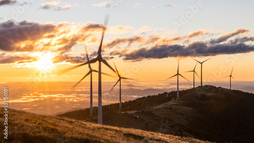 A group of wind mills on a mountain ridge in front of a morning sky photo