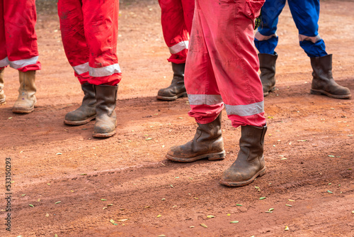 Group of an construction workers with fully PPE are standing on dirt route at working site during safety meeting. Selective focus at safety shoe part.