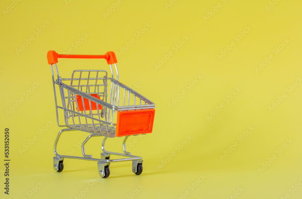 Metal shopping cart on a yellow background with a place to copy. A symbol of trade and sales. Metal shopping cart on a yellow background with a place to copy. A symbol of trade and sales.