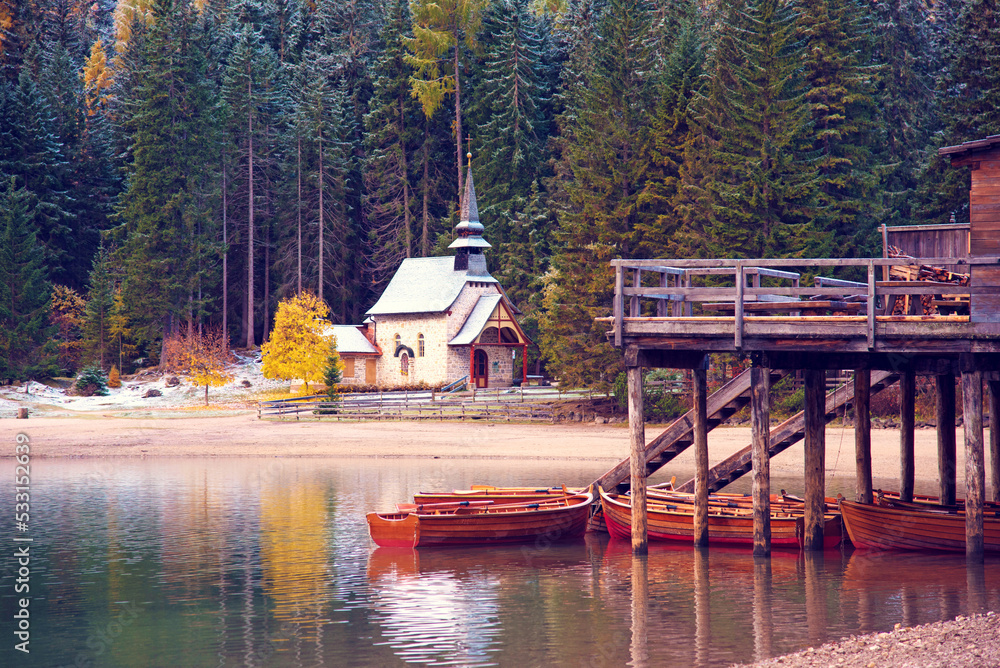 charming fascinating autumn landscape with a church and boats on the lake on Fanes-Sennes-Braies natural park in the Dolomites in South Tyrol, Alps, Italy.