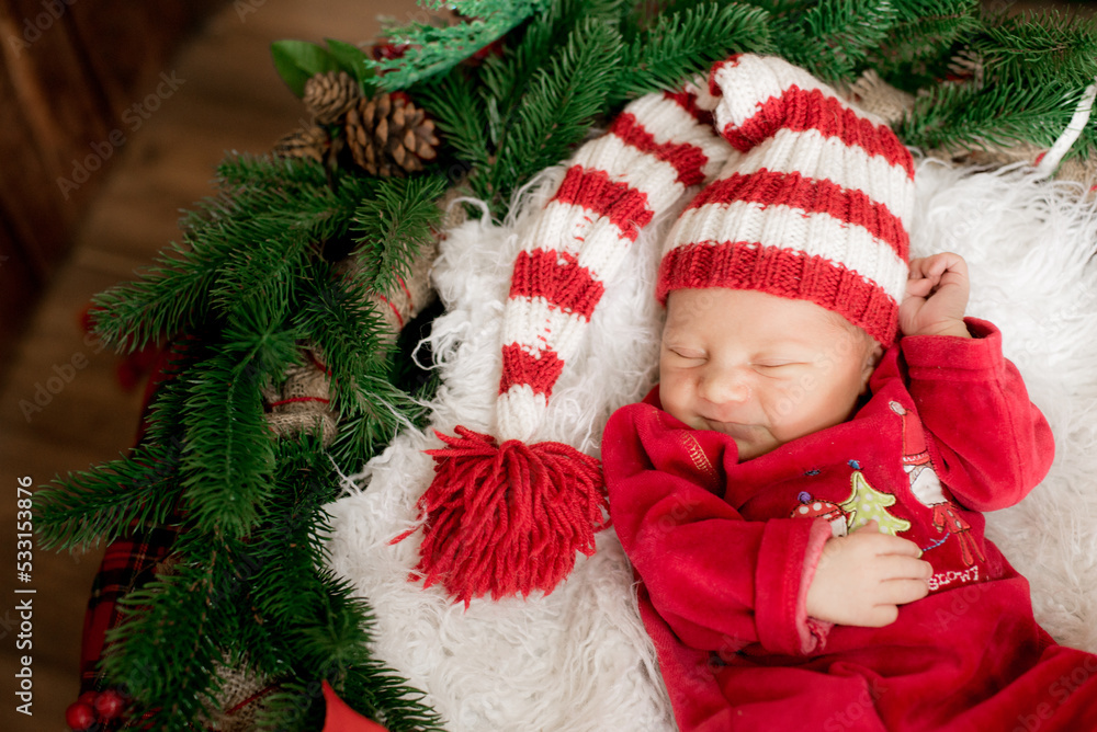 A cute little baby in a red suit and a cap is sleeping in a Christmas decoration. Christmas mood. Happy childhood. A cute little baby in a red suit and a cap is sleeping in a Christmas decoration. Christmas mood. Happy childhood.