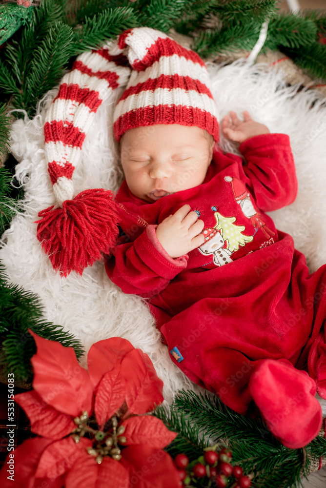 A cute little baby in a red suit and a cap is sleeping in a Christmas decoration. Christmas mood. Happy childhood.