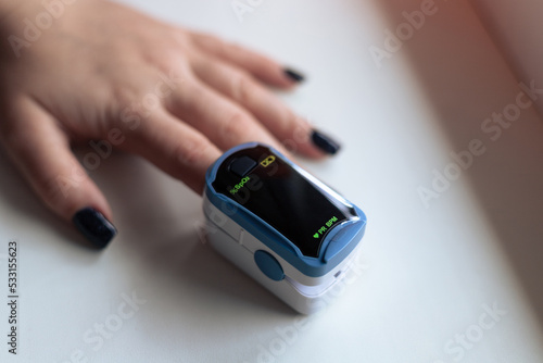 Pulse oximeter on a woman's hand. Pulse oximeter with blank display for your text. A woman is using a pulse oximeter. Measurement of pulse and the percentage of oxygen in the blood photo