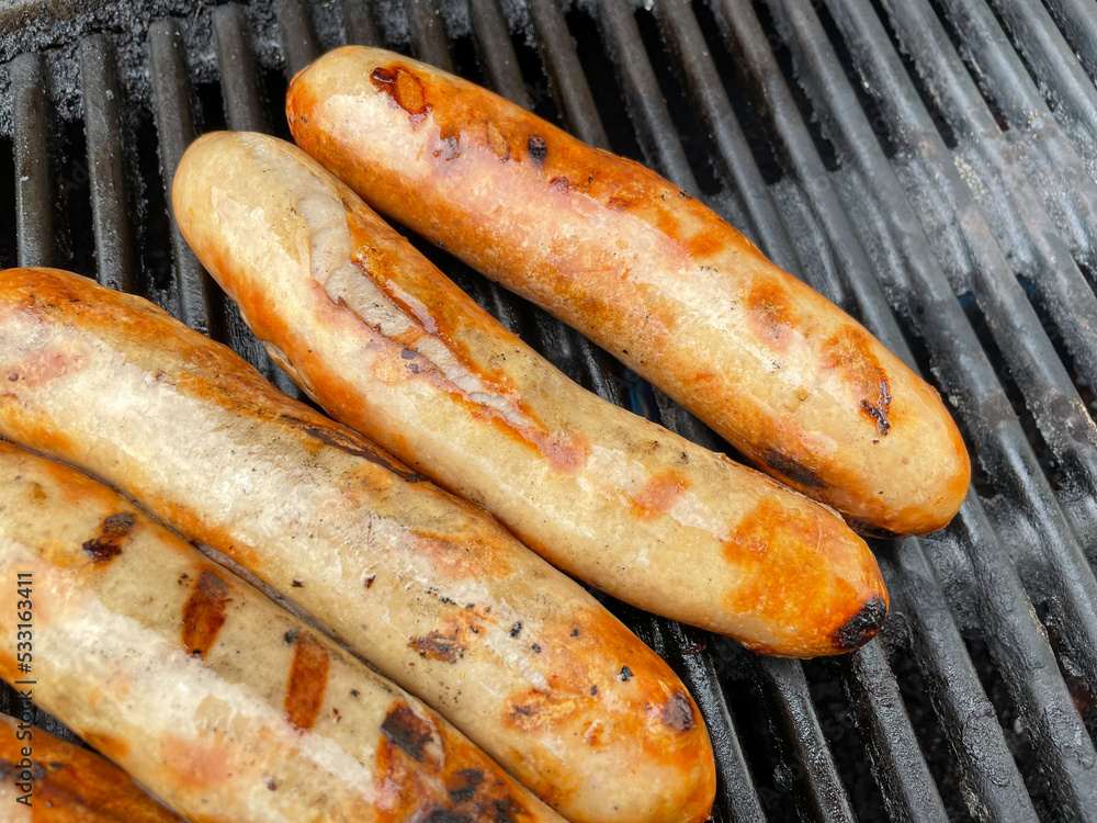 Mehrere braun gegrillte krosse Bratwürstchen auf dem schwarzen Grillrost eines Gasgrills bei einer Berbecue Party im Sommer Mehrere braun gegrillte krosse Bratwürstchen auf dem schwarzen Grillrost eines Gasgrills bei einer Berbecue Party im Sommer