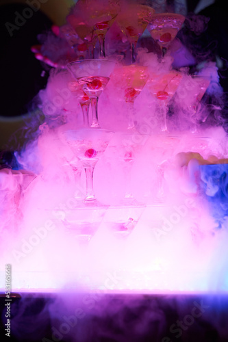 Bright glass pyramid of glasses with cherries, in smoke