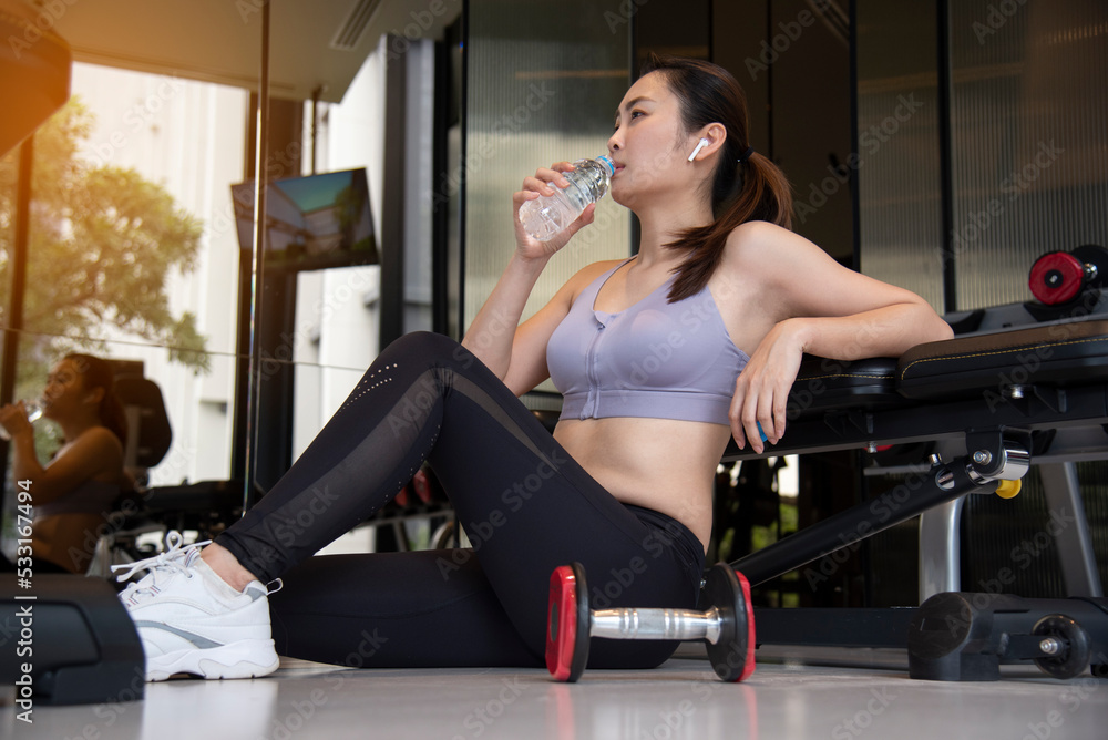 Sport woman sitting and resting after workout or exercise in fitness gym with protein shake or drinking water on floor. Relax concept. Sport woman sitting and resting after workout or exercise in fitness gym with protein shake or drinking water on floor. Relax concept.