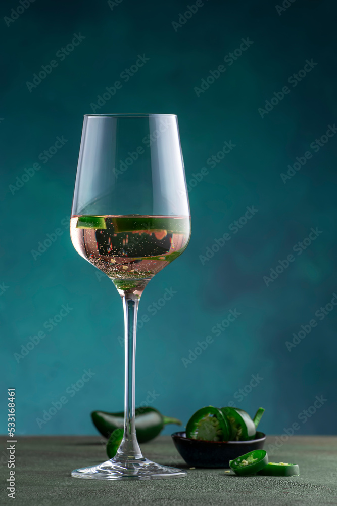 Rose pink wine with jalapeno pepper in wine glass, dark background