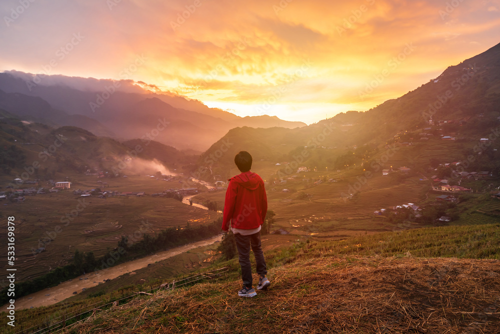 Young man traveler looking at beautiful landscape with mountains and green rice terraces view at sunset in Sapa, Vietnam