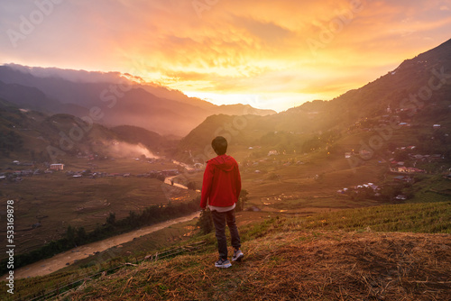 Young man traveler looking at beautiful landscape with mountains and green rice terraces view at sunset in Sapa, Vietnam