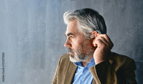 Foto Grey-haired mature man with hearing impairment using hearing aid