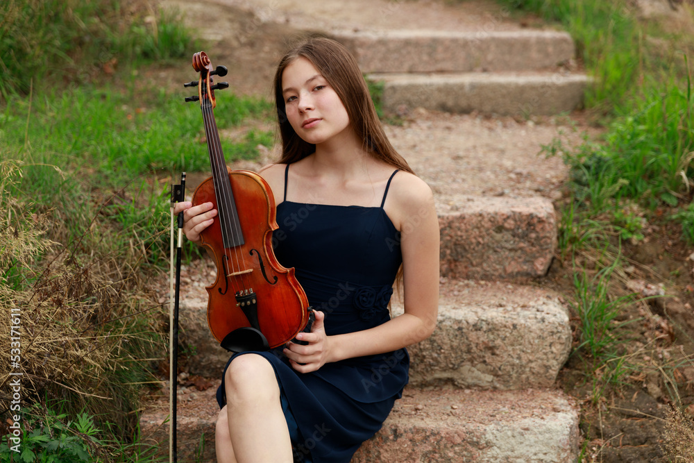 a beautiful girl with a violin sits on the steps in nature