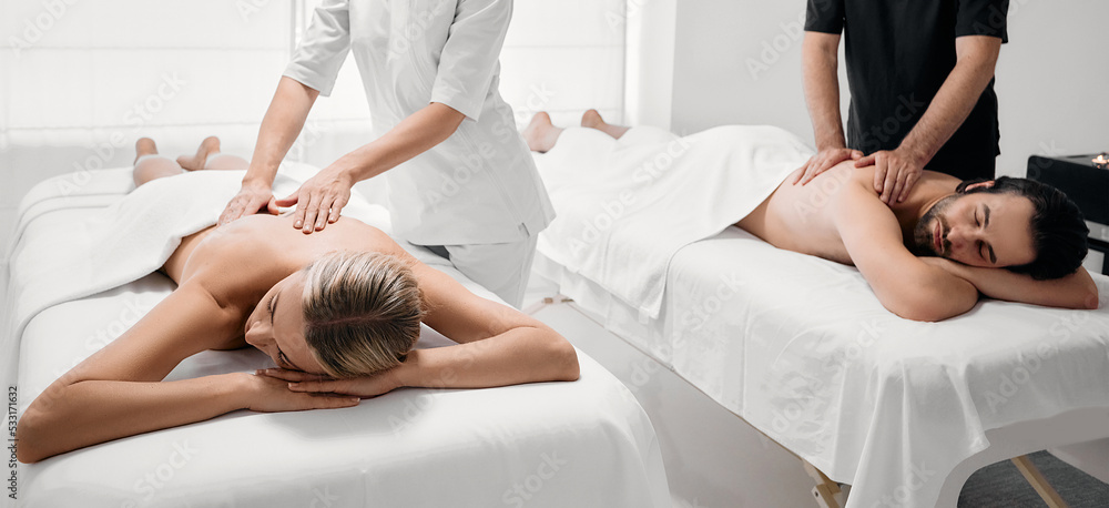 Fototapeta premium Beautiful couple getting back massage at spa salon. Handsome man and pretty woman relaxes while back massage