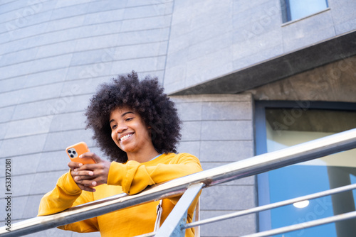 Happy millennial mixed race girl in the street of the city. Positive young african american woman web surfing with phone, searching information, shopping in online store outdoors.