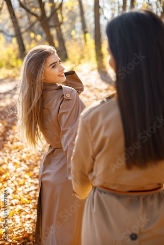 Two girls friends walking together in autumn park