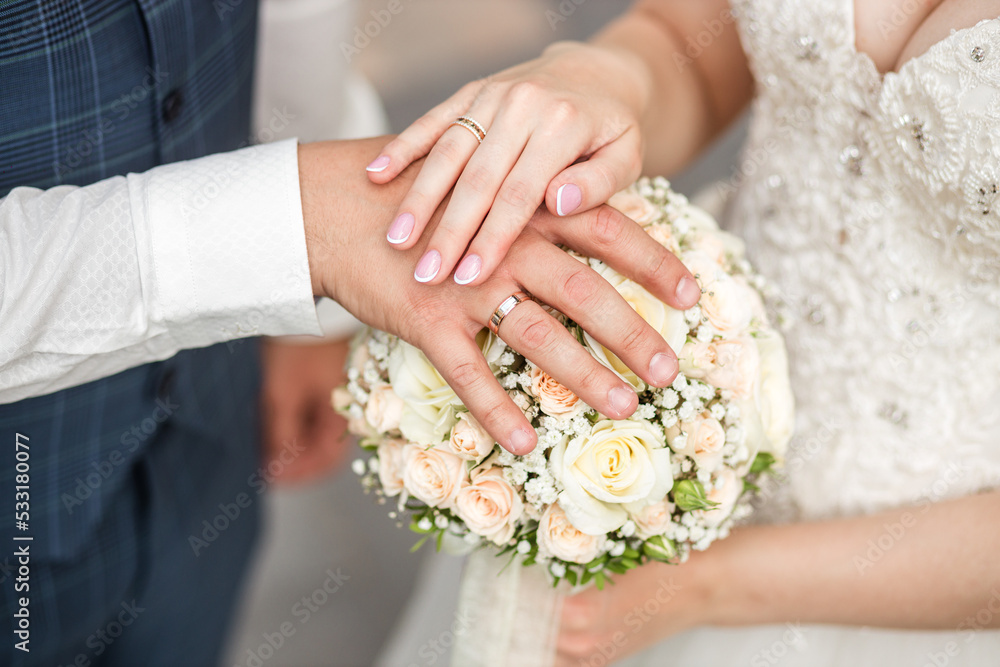the bride and groom put their hands with wedding rings on the wedding bouquet the bride and groom put their hands with wedding rings on the wedding bouquet