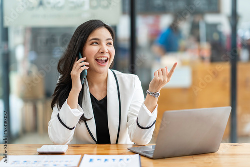 Wallpaper Mural Asian businesswoman happily chatting on the phone with a customer at a table in a modern office. Torontodigital.ca