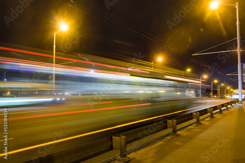 A blurred bus moves along the overpass in the evening..