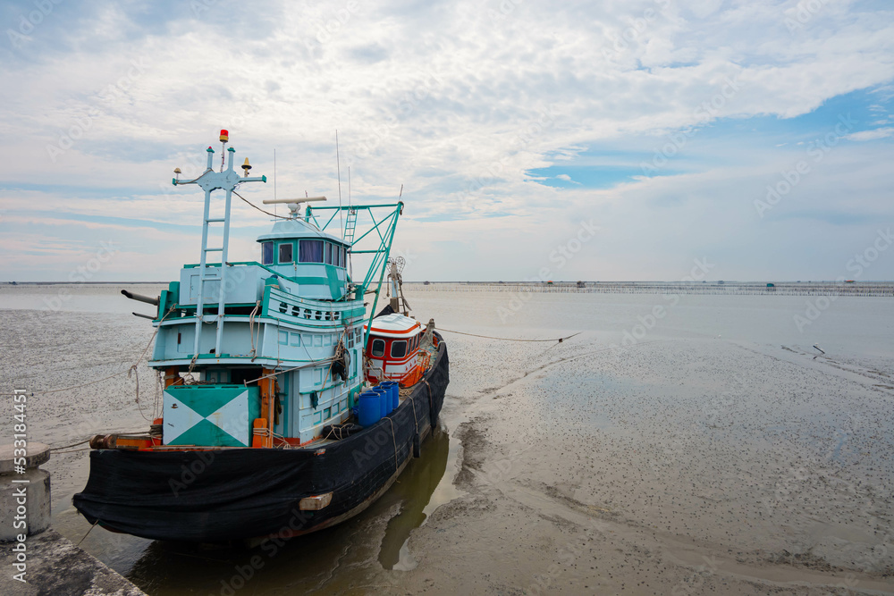 Boats get stranded during low tide with blue sky and clouds background