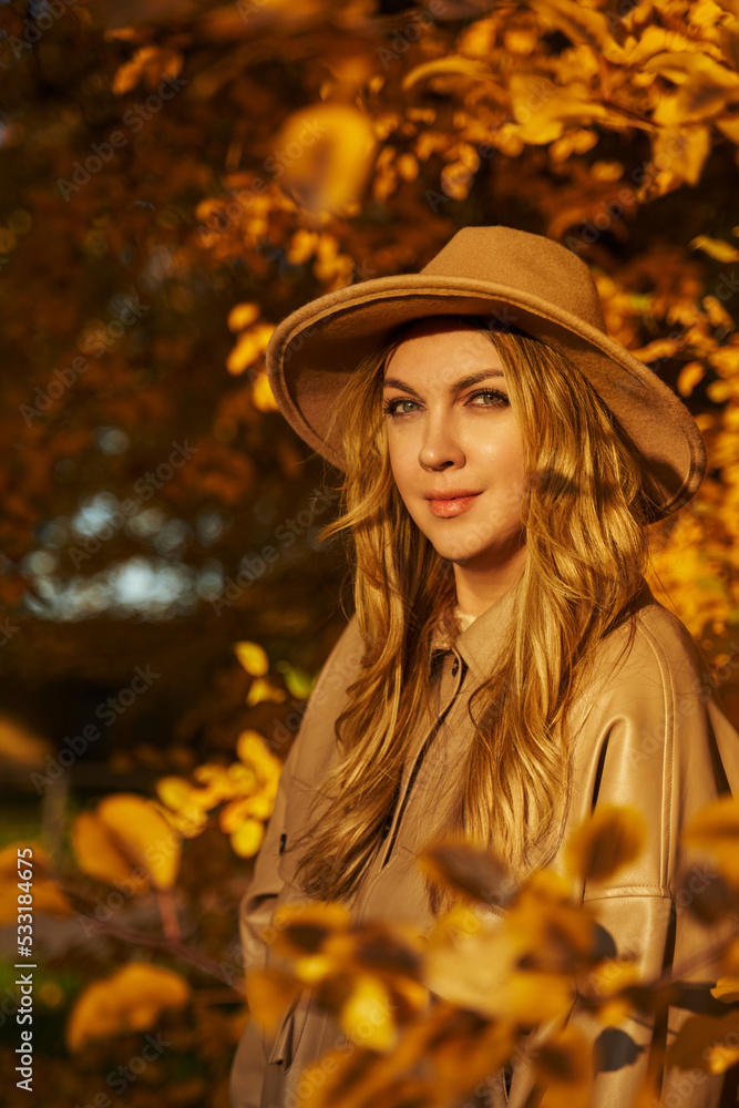 young beautiful woman in a hat and light clothes against the background of beautiful trees in light clothes. Warm autumn