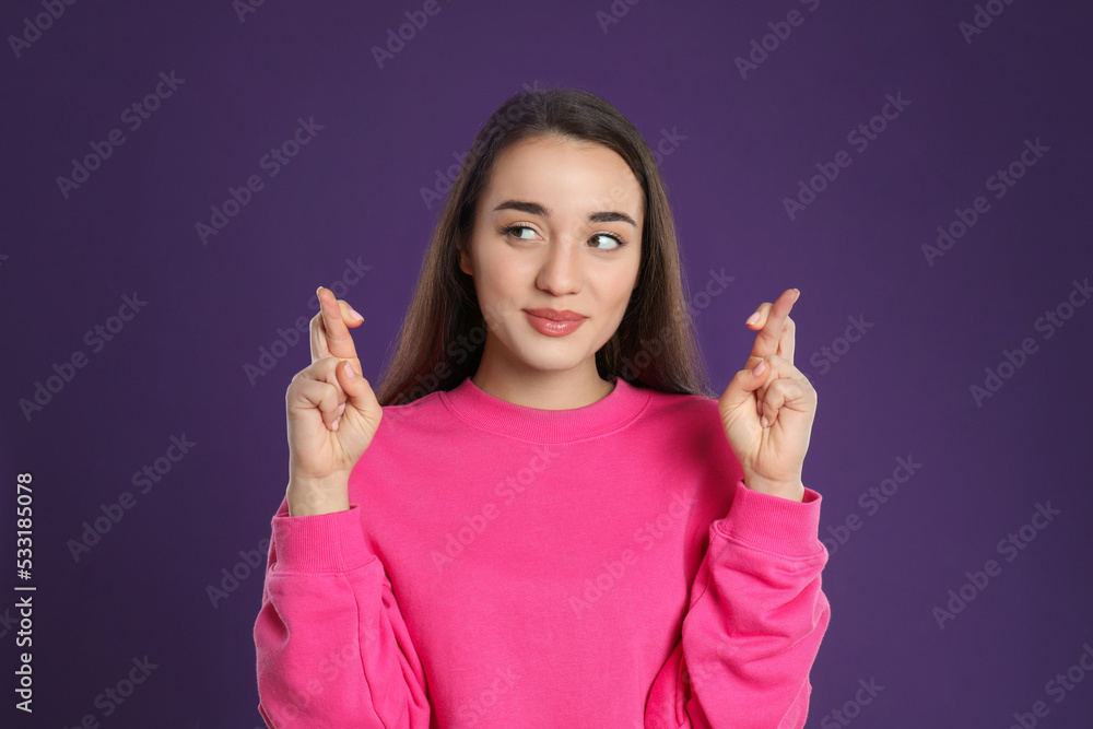 Woman with crossed fingers on purple background. Superstition concept Woman with crossed fingers on purple background. Superstition concept