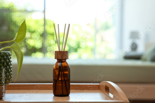 Aromatic reed air freshener near houseplant on wooden tray indoors. Space for text