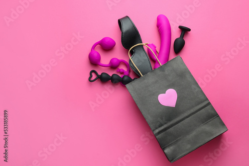 Shopping bag with different sex toys on pink background, flat lay. Space for text photo