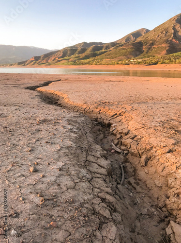 Beautiful landscape with setting sun: mountains, lake, cracked earth with stones -dried-up riverbend. Vertical image