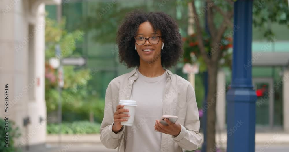 Outdoor shot of young curly hair woman walking on the street and looking to her phone intently, wearing glasses and casual cloth