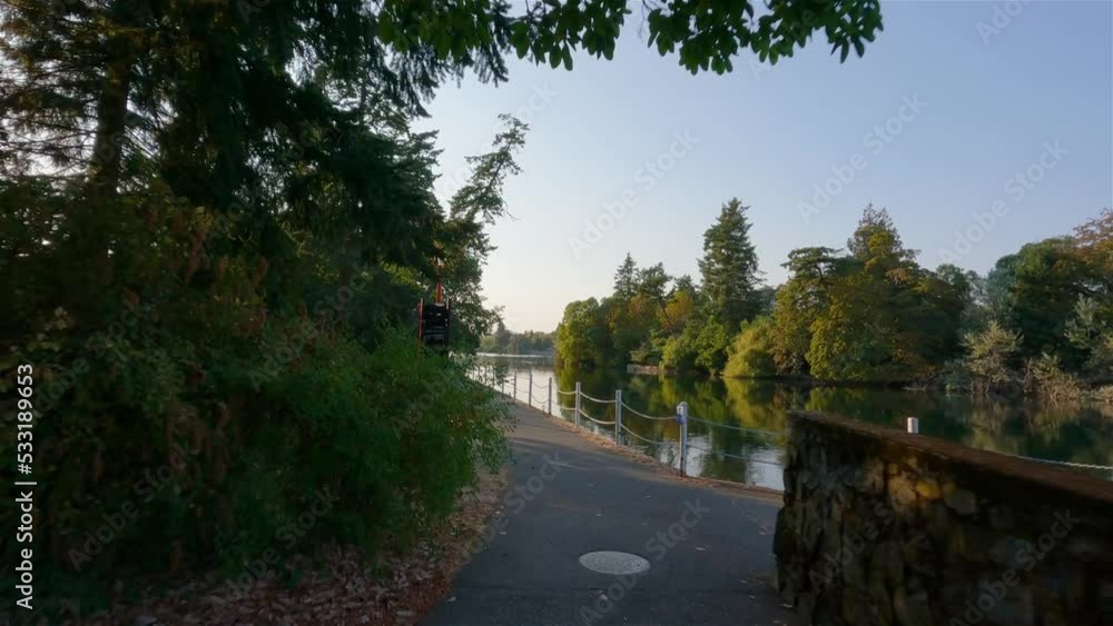 Trail in a park with vibrant green trees. Sunny summer sunset. Esquimalt Gorge Park, Victoria, Vancouver Island, British Columbia, Canada. Trail in a park with vibrant green trees. Sunny summer sunset. Esquimalt Gorge Park, Victoria, Vancouver Island, British Columbia, Canada.