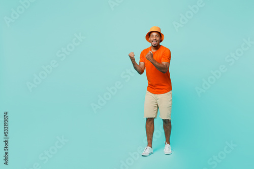 Full body happy young man of African American ethnicity 20s wear orange t-shirt hat doing winner gesture celebrate say yes isolated on plain pastel light blue cyan background People lifestyle concept