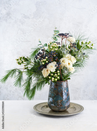 Beautiful winter bouquet in vase. Flower arrangement with roses, fir branches, winter berries, eucalyptus and eryngium. Christmas flower decoration.
