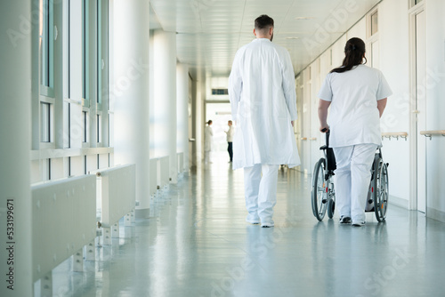 Doctor and nurse pushing wheelchair with woman patient in hospital photo