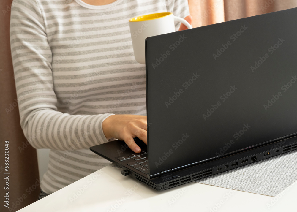 Fototapeta premium a woman sits at a white table in front of a black laptop and holds a cup in her hand