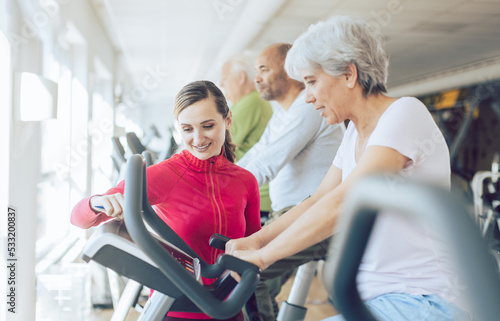 Fitness coach in gym helping senior people during cardio bike training
