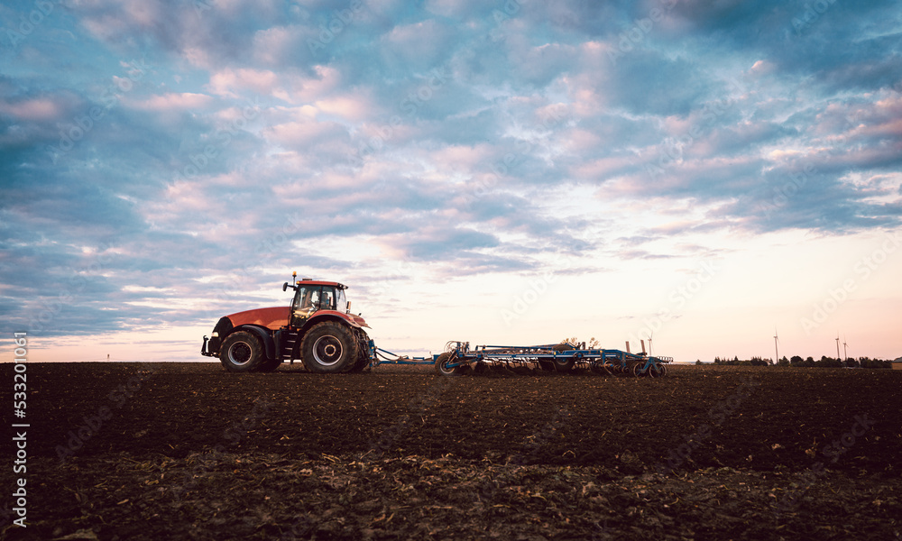 Fototapeta premium Tractor on field tilling the soil during sunset