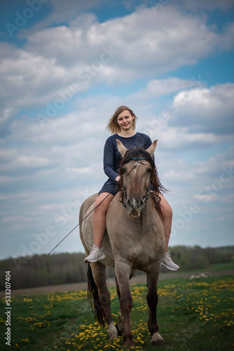 A young beautiful blonde girl trains a horse in the field.