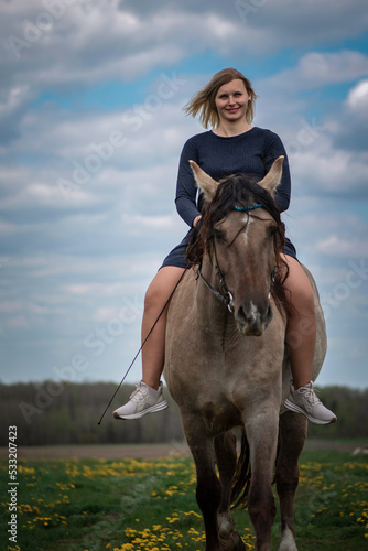 A young beautiful blonde girl trains a horse in the field.