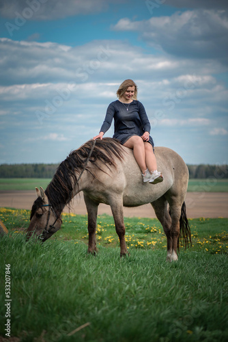 A young beautiful blonde girl trains a horse in the field.
