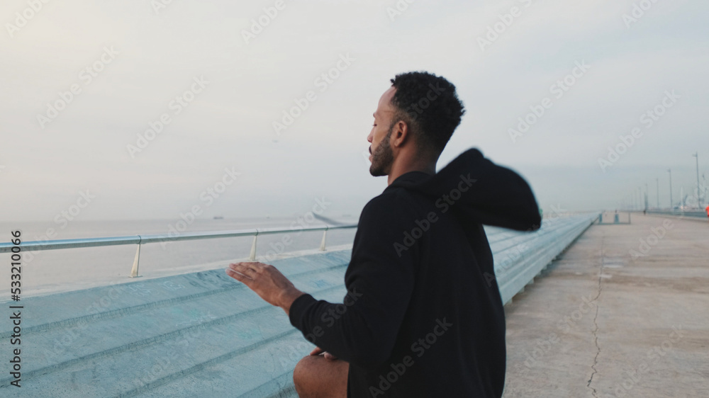 Young bearded male athlete doing warm-up, stretching legs before training while standing on the embankment Young bearded male athlete doing warm-up, stretching legs before training while standing on the embankment