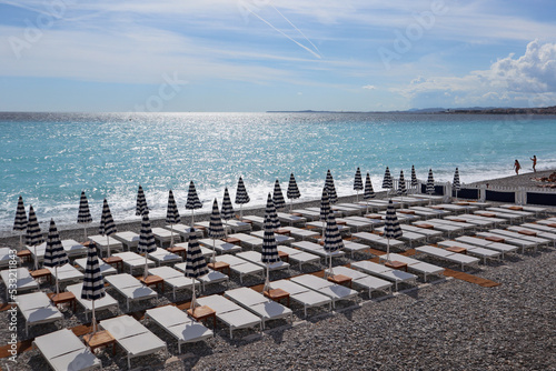 View of the beach with sun loungers and closed sun umbrellas in Nice, on the Mediterranean coast.