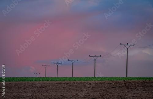 Autumn evening field with electric wire and poles and color sky after sunset