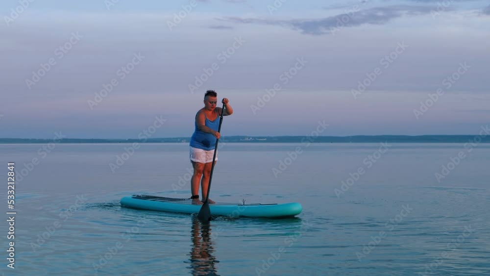 A short-haired woman swims on a SUP board before sunset A short-haired woman swims on a SUP board before sunset