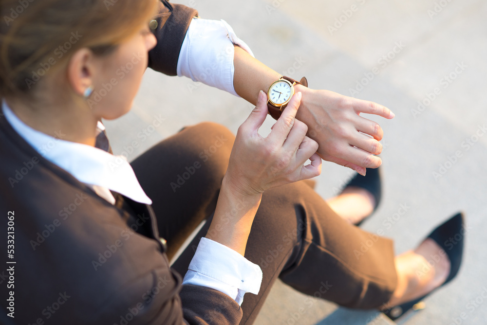 Young worried businesswoman looking at time on her wristwatch while sitting on stairs