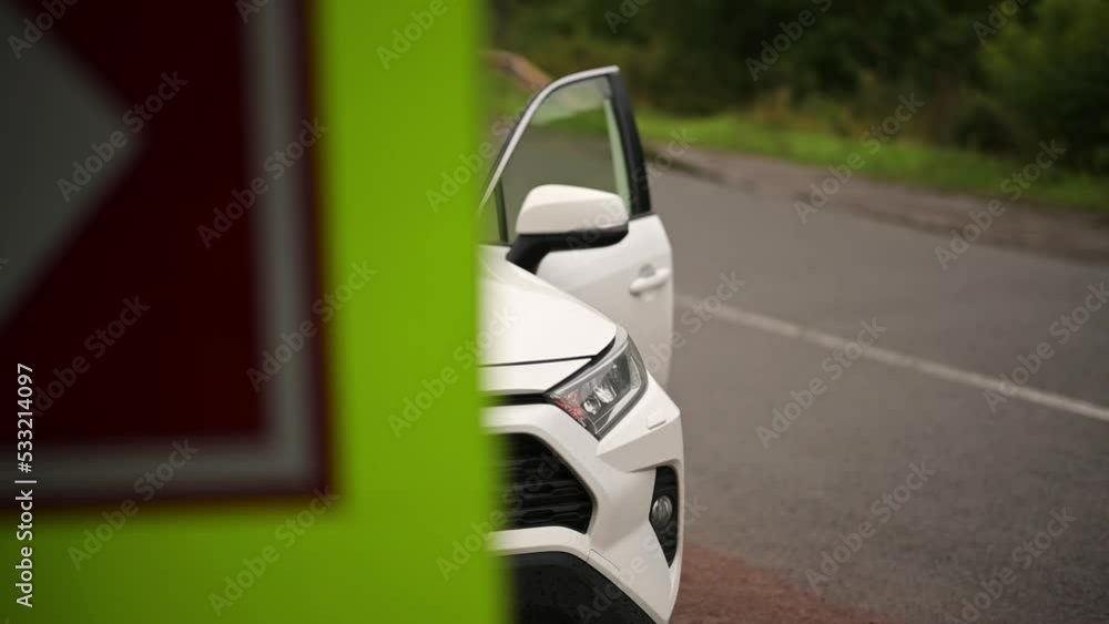 A white car is parked on the side of the road with the hazard warning