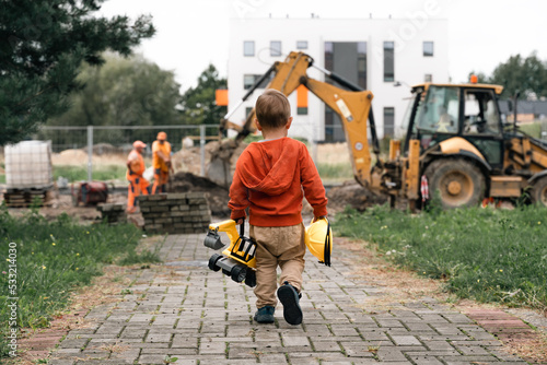 Child with excavator near construction site, dreams to be an engineer. Little builder. Education, and imagination, purposefulness concept