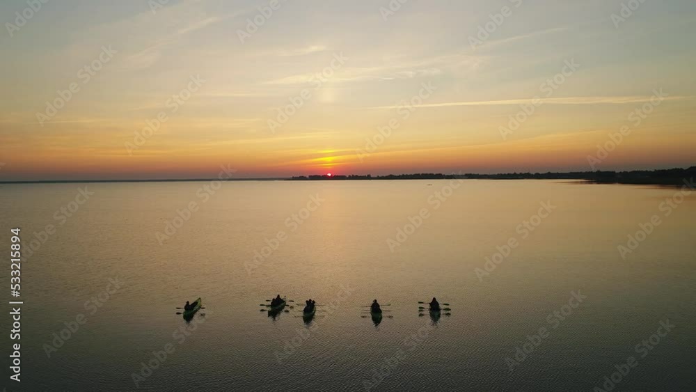 Five canoes with people stand on the water and wait for the sunrise. A large lake with a reflection of the colored sky. Five canoes with people stand on the water and wait for the sunrise. A large lake with a reflection of the colored sky.